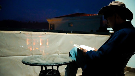 Man in cowboy hat reads book on balcony with privacy fence screen
